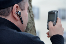 A security officer holding a cellphone and wearing an earpiece